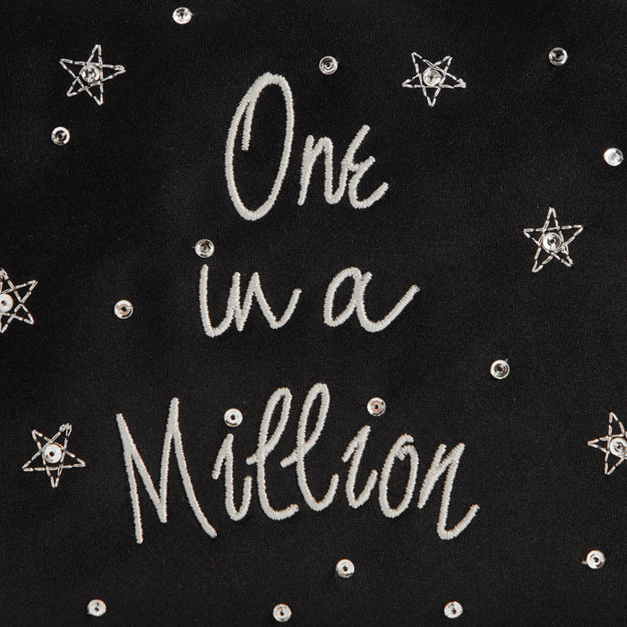 Close-up of black fabric with the words "One in a Million" embroidered in light grey thread and embellished with silver star-shaped sequins.