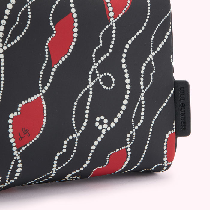 Close-up of a Lulu Guinness black handbag with a red and white pearl necklace print.