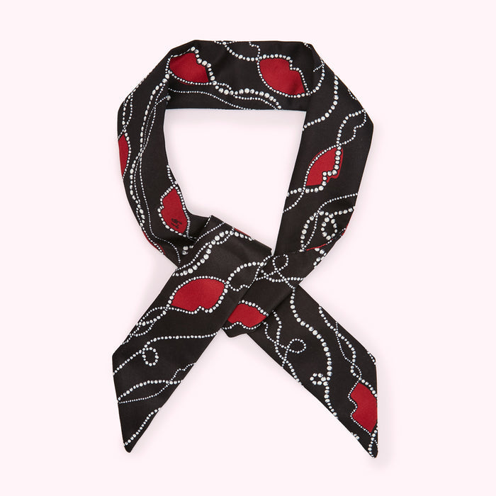 Black silk scarf with red hearts and white pearl detailing, tied in a knot.