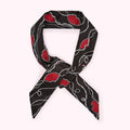 Black silk scarf with red hearts and white pearl detailing, tied in a knot.