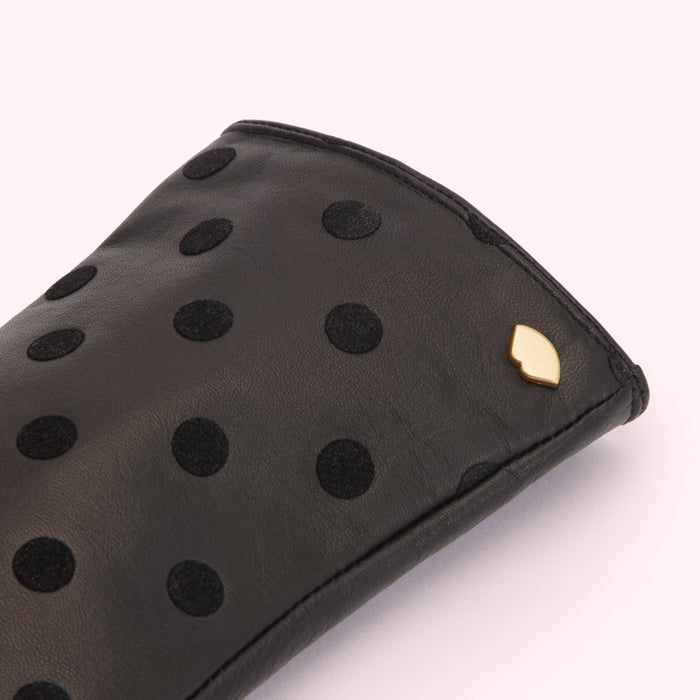 Close-up of a black leather glove with black polka dots and a small gold logo.