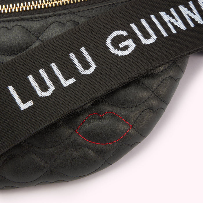 A close-up detail image of the lip shaped quilting, red lip stitching and branded 'Lulu Guinness strap on a black leather belt bag.