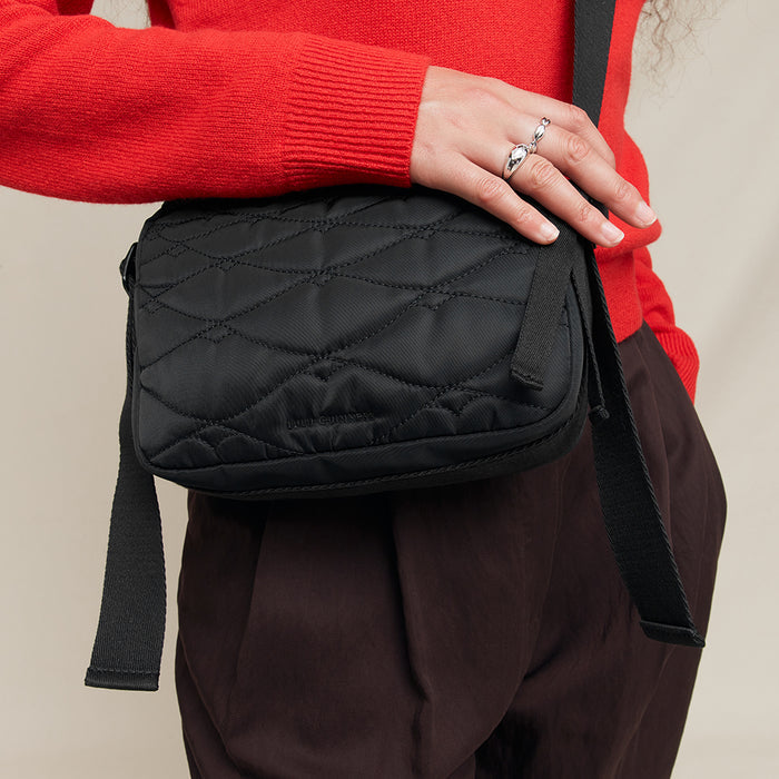 Person holding a black quilted crossbody bag with a red sweater and brown pants.