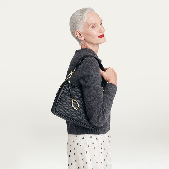 Woman holding a black quilted handbag against a light gray background
