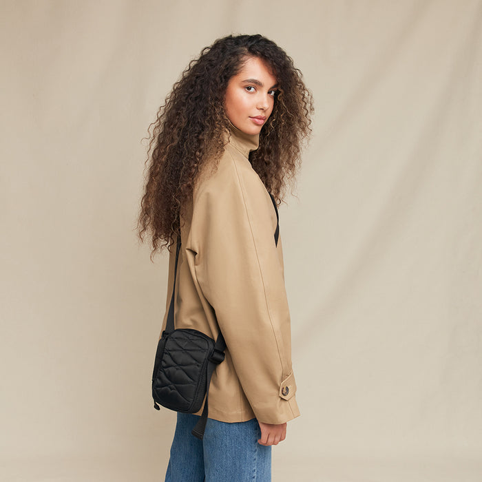 Woman wearing a beige jacket with a black quilted bag on a beige background
