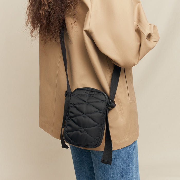Person wearing a beige coat with a black quilted crossbody bag on a beige background