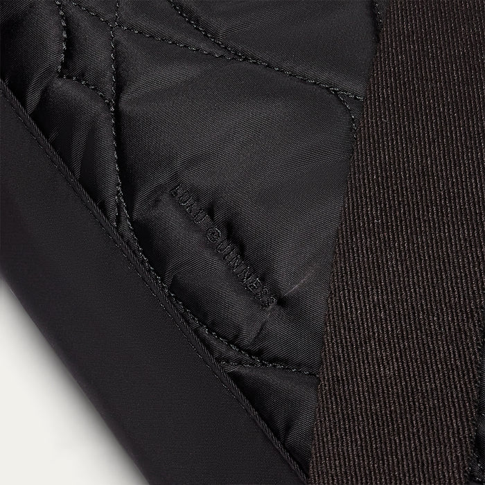 Close-up of a black quilted shoulder bag with a embroidered 'Lulu Guinness' logo on a light gray background