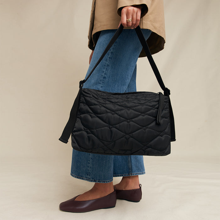 Person holding a black quilted bag against a beige background