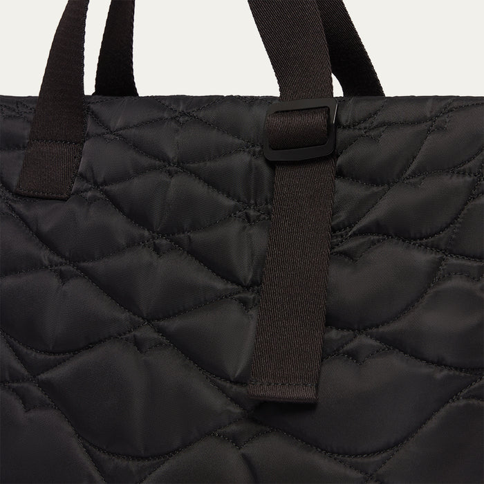 Close-up of a black quilted tote bag with woven straps and lip shaped quilting on a light gray background