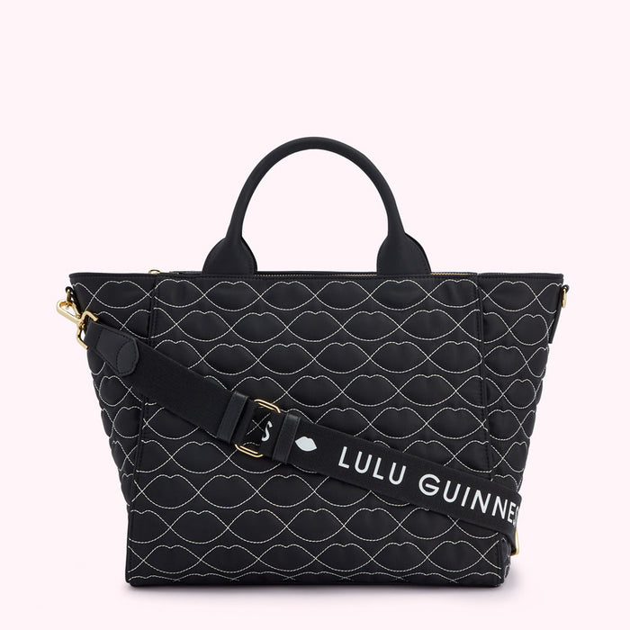 Black quilted tote bag with white lip print and detachable shoulder strap. The strap has the Lulu Guinness logo.