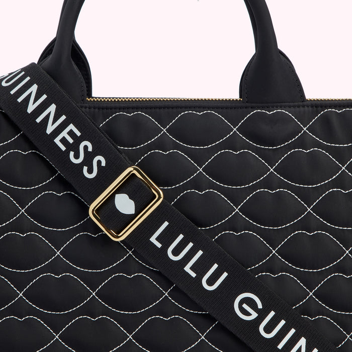 Close-up of a black Lulu Guinness bag with a quilted lip print and a black strap with white "Lulu Guinness" lettering.