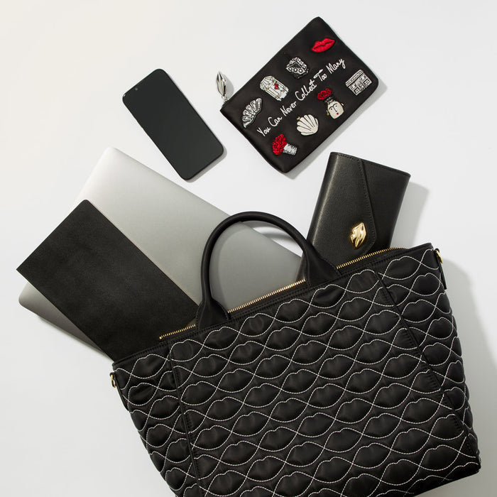 A black quilted tote bag sits on a white background with a laptop, phone, wallet, and cosmetic bag inside.
