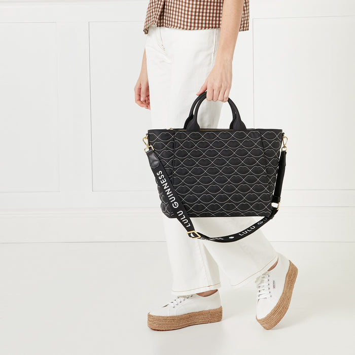 Woman holding a black Lulu Guinness tote bag with a lip print against a white background.
