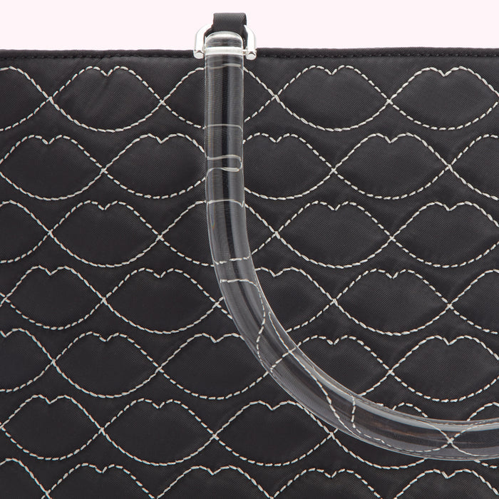 Close-up of a black quilted handbag with a clear acrylic handle; the quilting pattern is of repeated lip shapes.