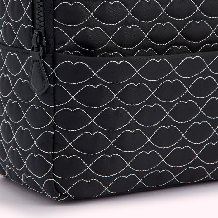 Close-up of a black quilted backpack with a lip-shaped pattern.