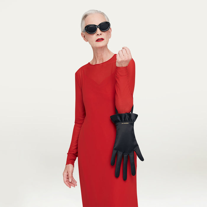 Woman in a red dress holding a black satin hand-shaped handbag against a gray background