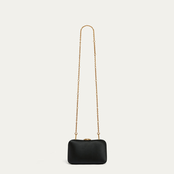 Black satin clutch bag with a gold chain on a light beige background