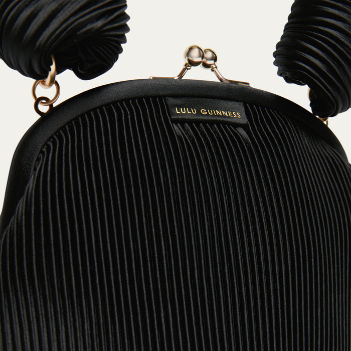 Black pleated satin handbag with 'Lulu Guinness' label on a light gray background