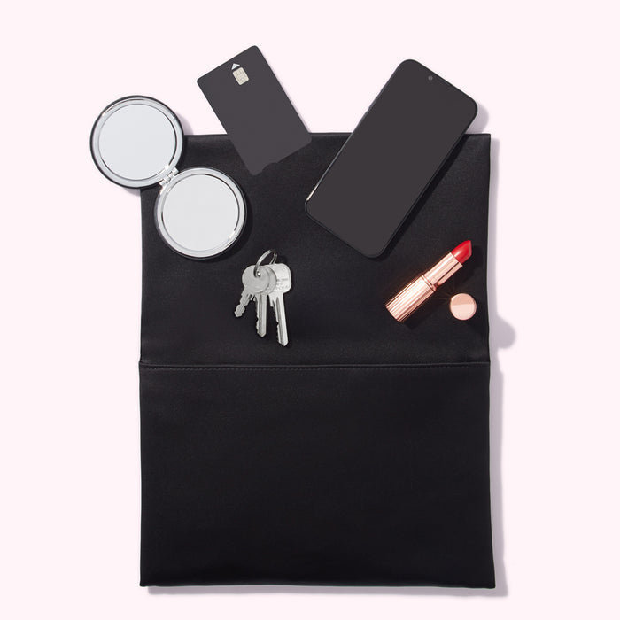 A black clutch open to reveal a smartphone, compact mirror, keys, credit card, and lipstick.