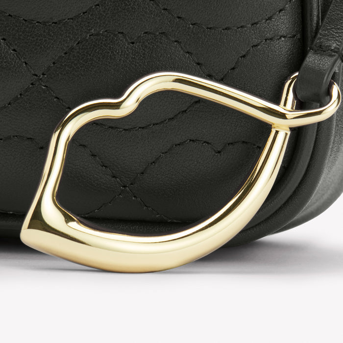 Close-up of a black quilted handbag with a gold lip-shaped detail.