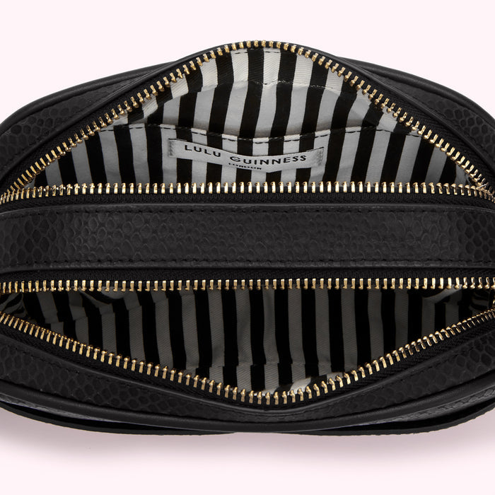 Interior of a black Lulu Guinness crossbody bag with gold zippers and a black and white striped lining.