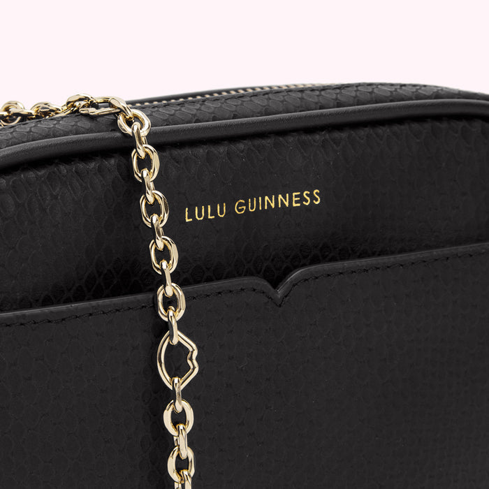 Close-up of a black Lulu Guinness crossbody bag with a gold chain strap.