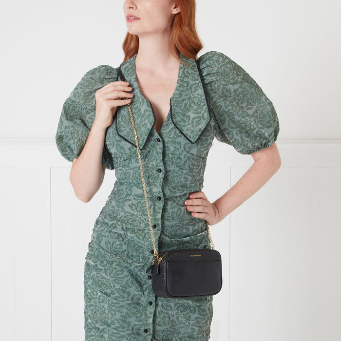 Woman in sage green dress with black crossbody bag.