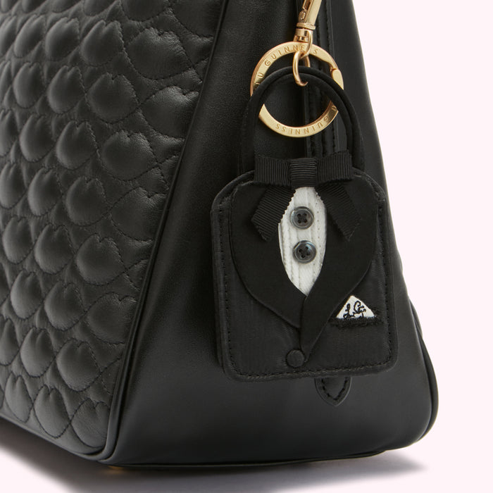 Close-up of a black quilted leather handbag with a tuxedo-shaped keychain attached.