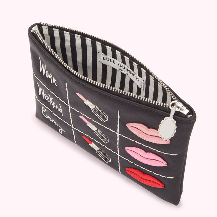 Black Lulu Guinness makeup bag with lipstick and lip designs and "Work," "Weekend," and "Evening" labels embroidered on the front. The interior is black and white striped.