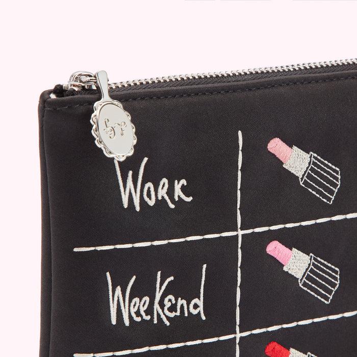 Close-up of a black makeup bag with embroidered lipstick designs and the words "Work" and "Weekend," featuring a silver zipper and charm.