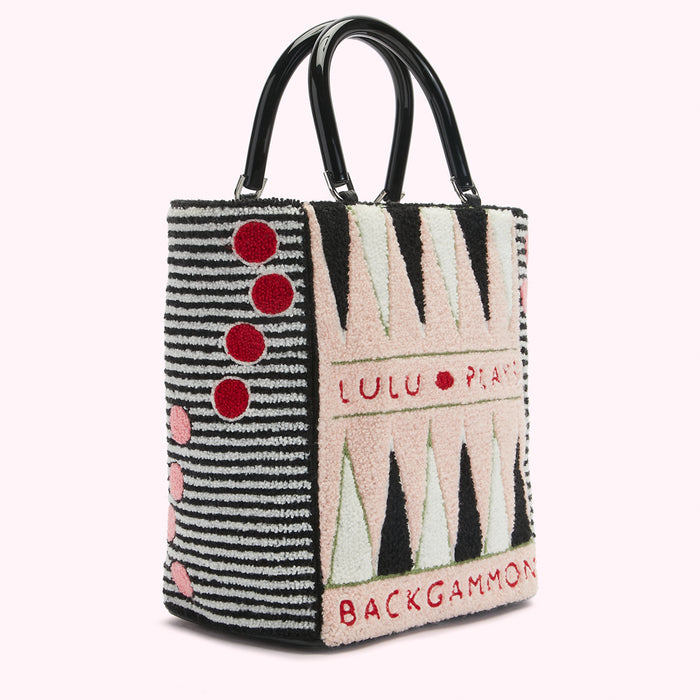 Side view of a Lulu Guinness Backgammon tote bag with black handles, a black and white striped section, and a pink and black backgammon board design.