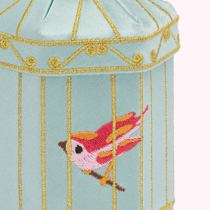 Close-up of a light teal birdcage-shaped object with gold embroidery, featuring a pink and orange bird.