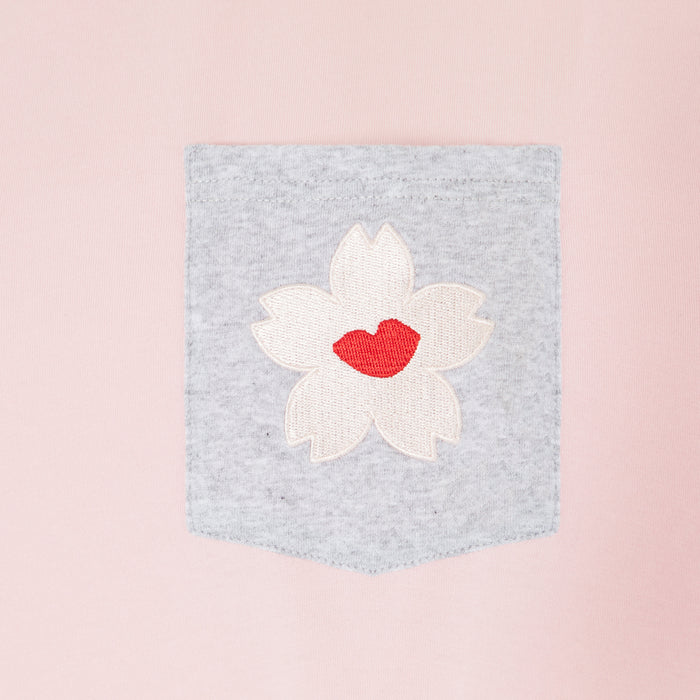 Close-up of a pale pink garment with a grey pocket featuring an embroidered white cherry blossom with a red lip in the centre.