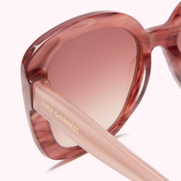 Close-up of Lulu Guinness sunglasses with a pink ombre lens and blush pink temples.
