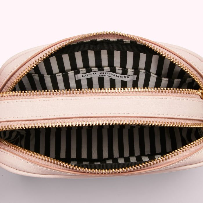 Inside of a pale pink Lulu Guinness London crossbody bag with gold zippers and a black and white striped interior.