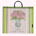 Large reusable tote bag with pink and green striped background, featuring a drawing of pink roses in a light green urn. The bag has green trim and black handles. The artist's names, "Annabel Pearl x Lulu Guinness," are printed on the bag.