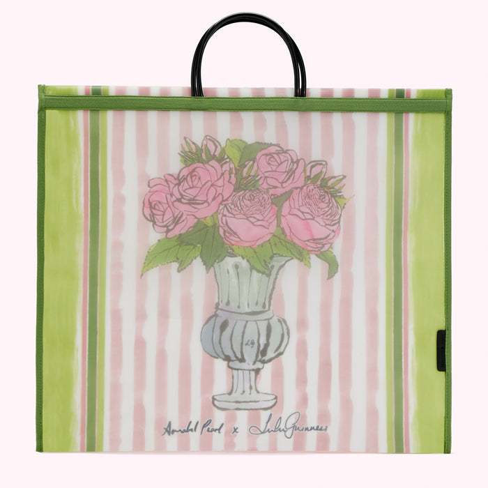 Large reusable tote bag with pink and green striped background, featuring a drawing of pink roses in a light green urn. The bag has green trim and black handles. The artist's names, "Annabel Pearl x Lulu Guinness," are printed on the bag.