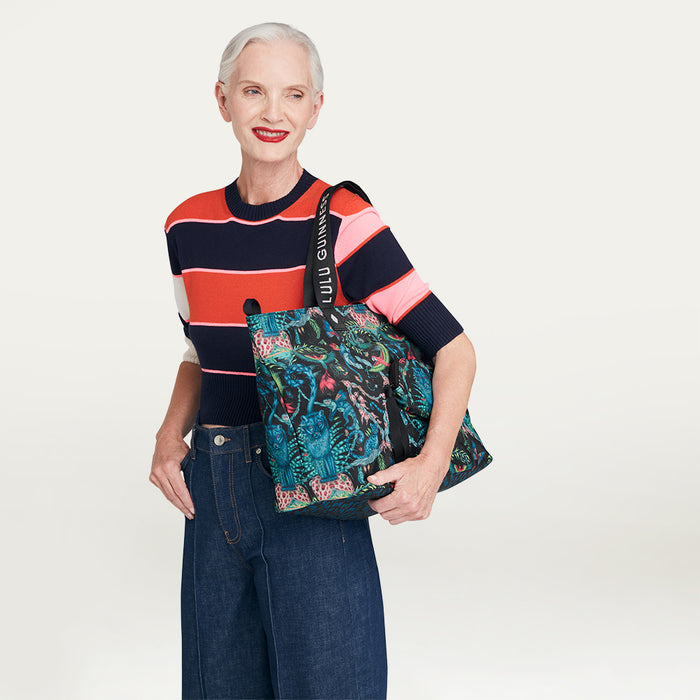 Woman holding a colorful Lulu Guinness x Emma Shipley printed tote bag against a plain background