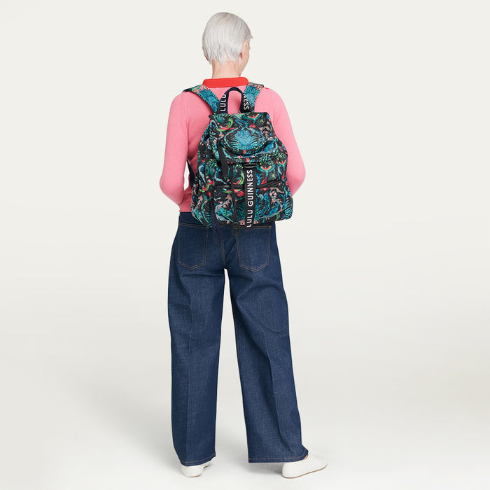 Person wearing a colorful Lulu Guinness x Emma Shipley printed backpack with a visible brand logo on a plain background
