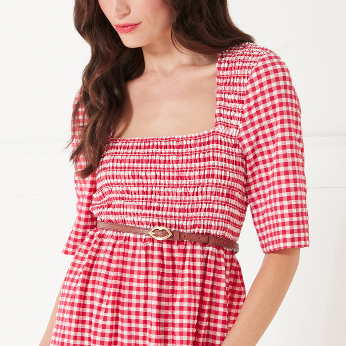 Close up image of a women wearing a red gingham print dress and a tan brown leather belt with a gold lip buckle on her waist.