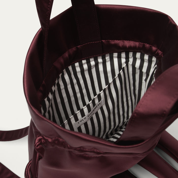 Close-up of a burgundy satin backpack with a striped lining on a white background