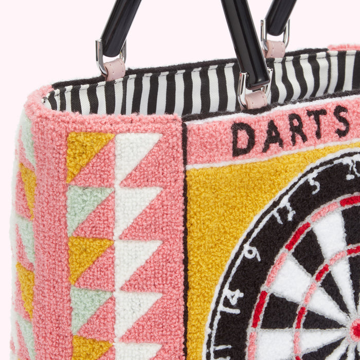 Close-up of a pink and yellow handbag with a dartboard design, black handles, and a black and white striped interior.