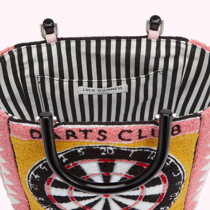 Close-up view of the inside and outside of a Lulu Guinness Darts Club tote bag. The interior is black and white striped fabric with a label reading "Lulu Guinness London." The exterior is a pink, yellow and white textured fabric depicting a dartboard. The bag has black handles.