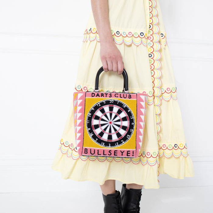 Woman holding a pink and yellow handbag with a dartboard design against a white background.