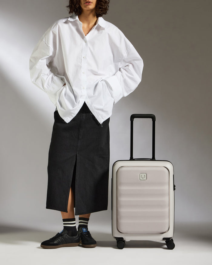 a man in a white shirt and black skirt standing next to a suitcase