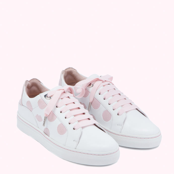 Pair of white leather sneakers with pink polka dots and pink laces against a pink background.