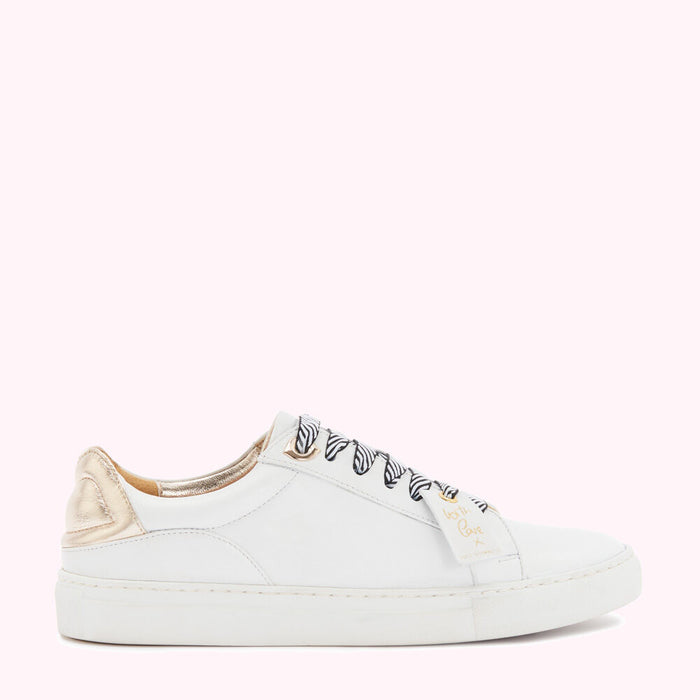 White leather sneakers with gold heel detail and zebra-print laces against a pink background.