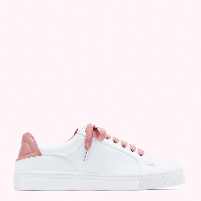 White leather sneaker with dusty rose accents and laces on a pink background.
