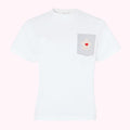 White t-shirt with grey pocket featuring a white flower applique and a red heart detail, on a pink background.
