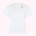 White short-sleeved t-shirt with pink cherry blossom and red lip print near neckline against pink background.